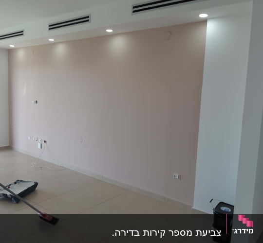 קיר צבוע בצבע ורוד בהיר עם כלי צביעה על הרצפה